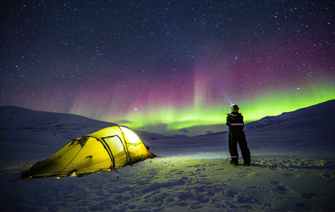 homme qui regarde des aurores boréales à coté de sa tente