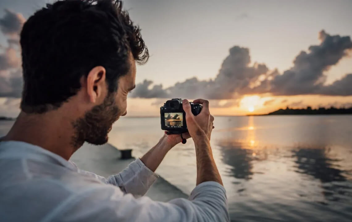 homme avec un appareil photo dans les main au couché du soleil