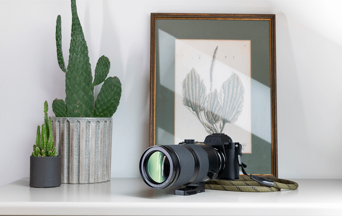 Objectif Leica SL 100-400mm F/5-6.3 sur table blanche avec fond blanc et tableau